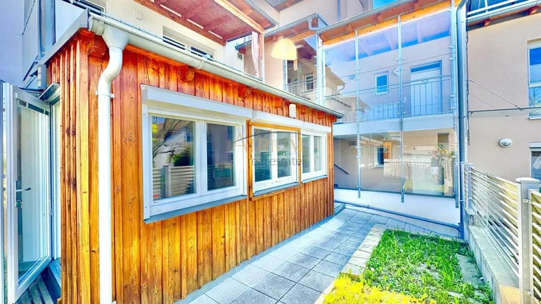 Außenbereich mit Holzverkleidung, gepflastertem Weg und Blick auf die moderne Glasfassade.