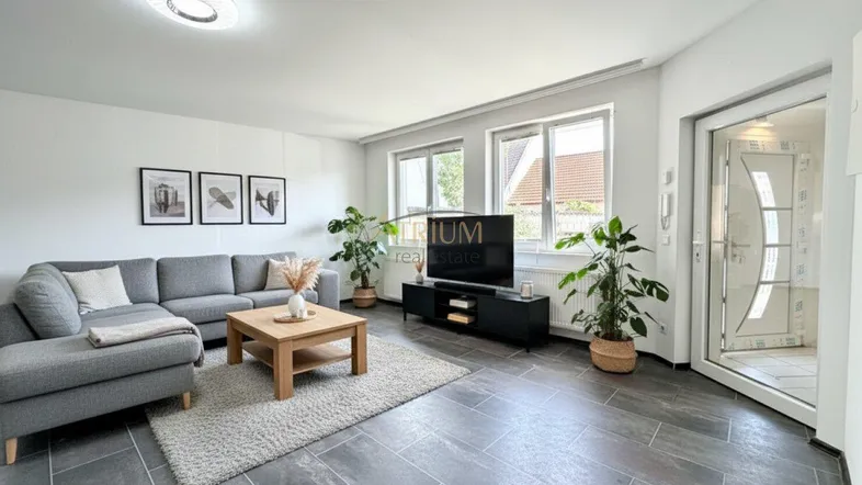 Helles Wohnzimmer mit modernem Sofa, Holztisch und dunklen Fliesen, durch große Fenster gut belichtet.