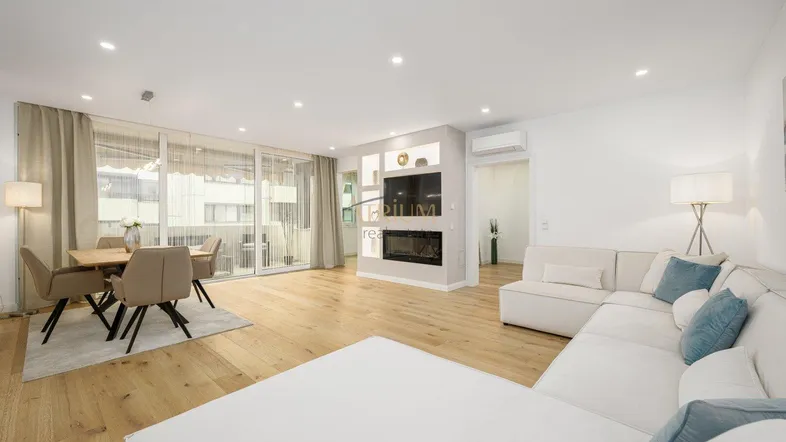 Helles Wohn- und Esszimmer mit modernem Sofa, Kamin und Zugang zu einem Balkon.