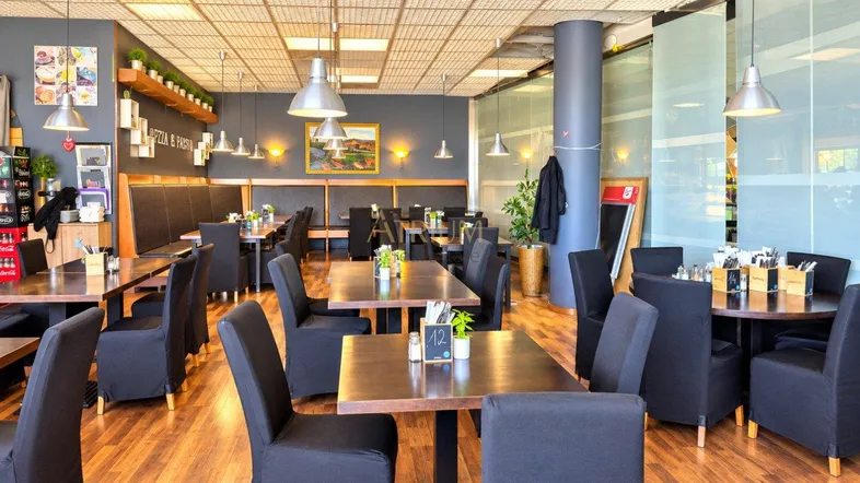 Geräumiger Restaurant-Essbereich mit Holzböden, modernen Tischen und bequemen Stühlen, hell beleuchtet durch große Fenster.