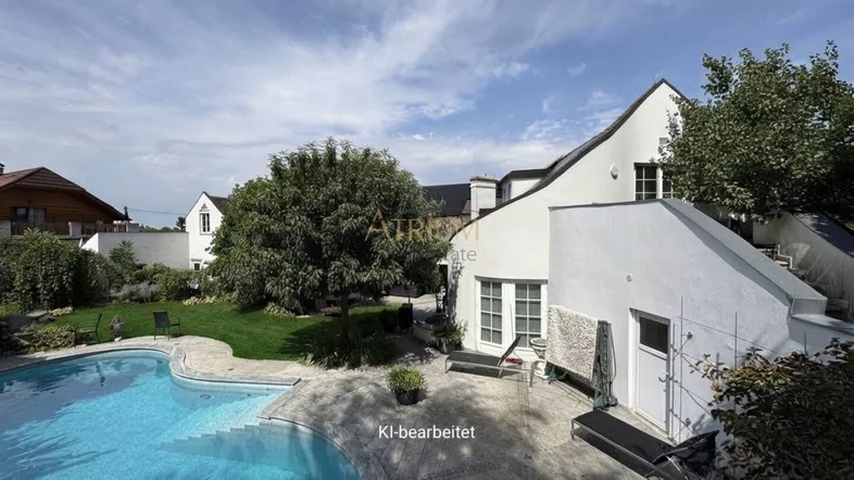 Großer Außenbereich mit geschwungenem Pool, gepflegtem Rasen und weißer Hausfassade unter blauem Himmel.