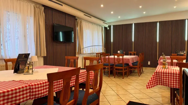 Gemütlicher Restaurant-Speisesaal mit karierten Tischdecken, Holzstühlen, Fliesenboden und einem Fernseher an der Wand.