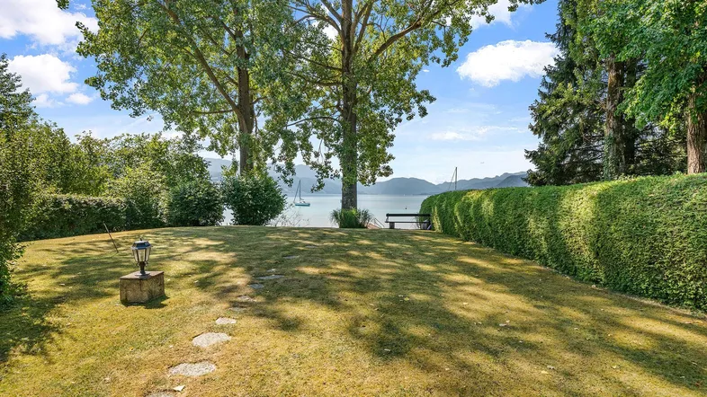 Großer gepflegter Gartenbereich mit Rasenfläche, hohen Bäumen und direktem Blick auf den See.