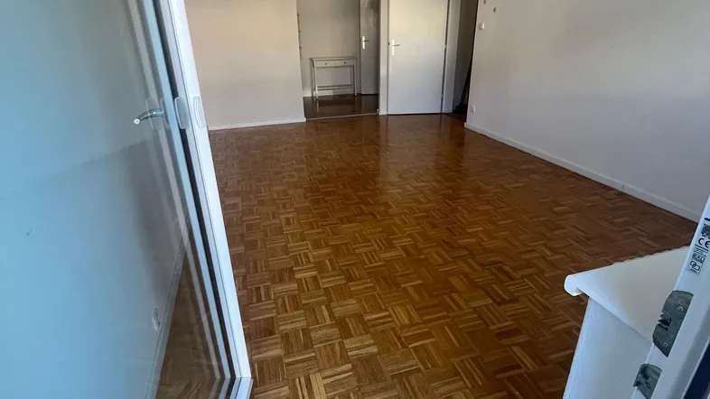 Helles Wohnzimmer mit Fischgrätparkettboden und Zugang zu einem Balkon oder einer Terrasse.
