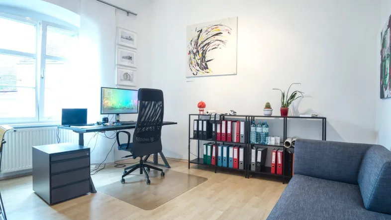 Helles Büro mit modernem Schreibtisch, ergonomischem Stuhl, Regalsystem und einem bequemen Sofa.