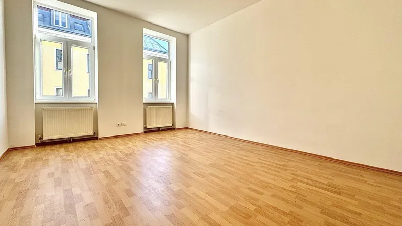 Helles Zimmer mit Holzparkettboden und zwei großen Fenstern, ideal als Wohn- oder Schlafzimmer.