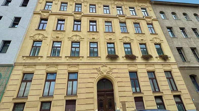 Historische gelbe Fassade eines Altbaus mit vielen Fenstern und dekorativen Stuckelementen.