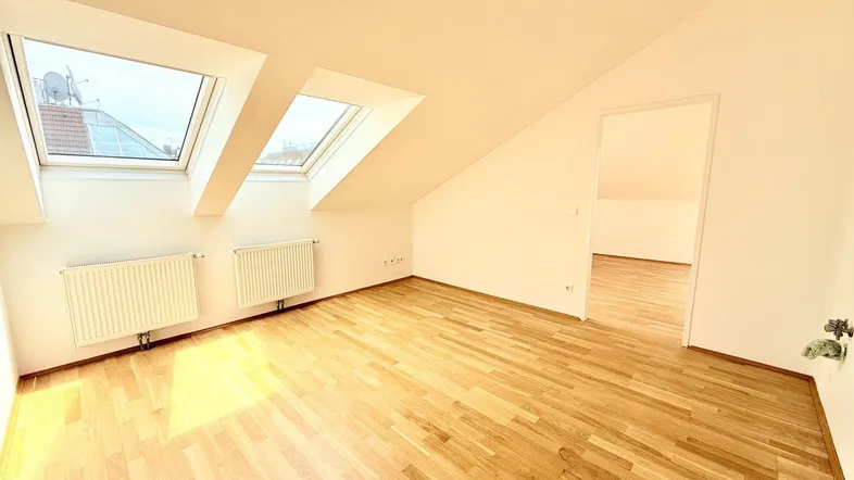 Helles Dachgeschosszimmer mit schrägen Wänden, zwei Dachfenstern und hellem Holzparkettboden.