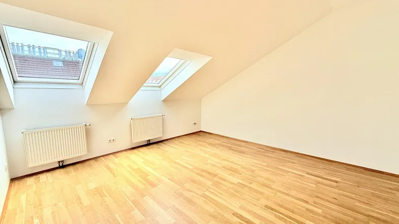 Heller Raum mit Dachschrägen, Parkettboden und zwei Dachfenstern, ideal als Wohn- oder Schlafzimmer.