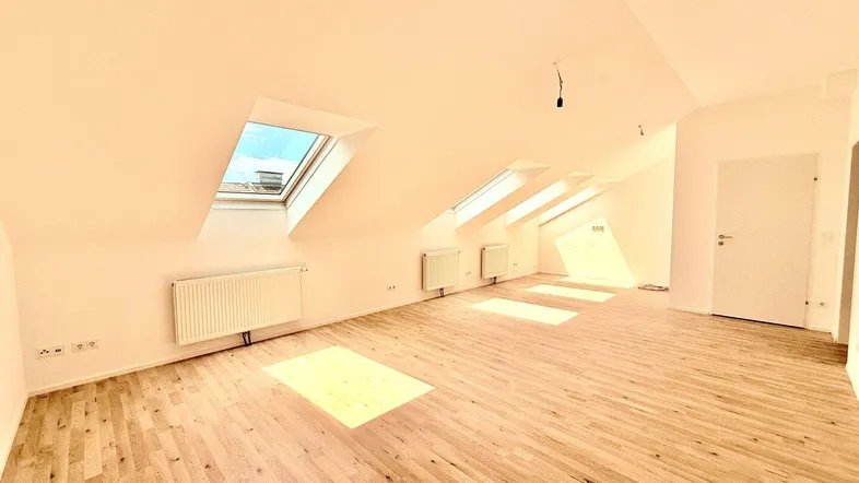 Helles Dachgeschosszimmer mit Holzfußboden, schrägen Decken und mehreren Dachfenstern, die viel Licht hereinlassen.