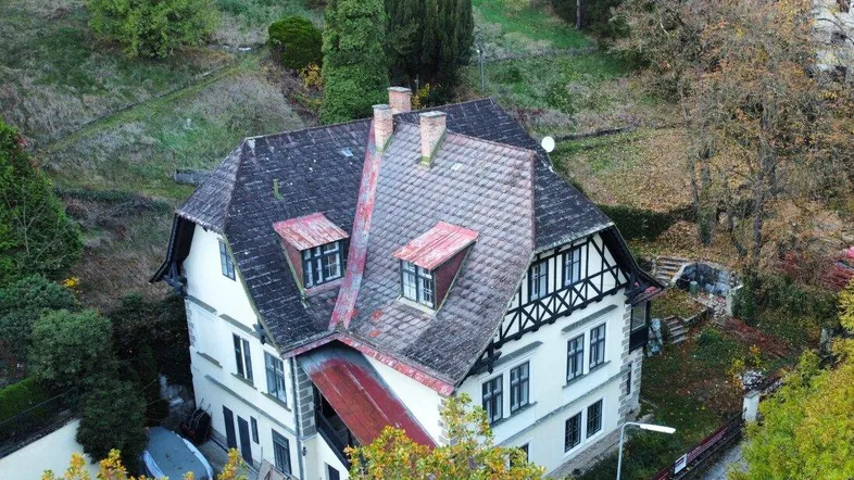 Luftaufnahme einer historischen Villa mit Satteldach und Fachwerkelementen, umgeben von herbstlicher Natur.