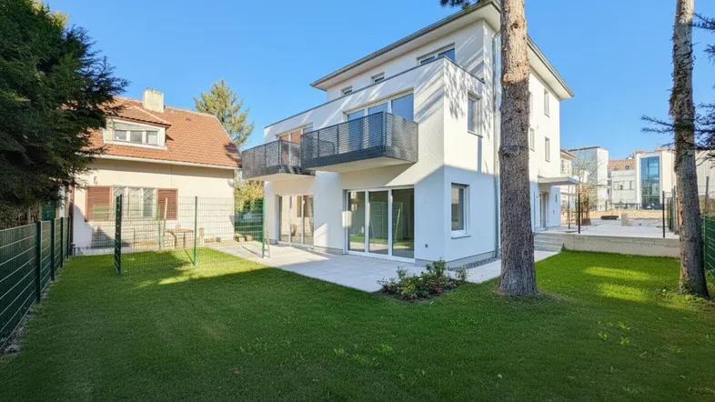Modernes Wohnhaus mit weißer Fassade, Balkonen und einer gepflegten Rasenfläche mit Terrasse.