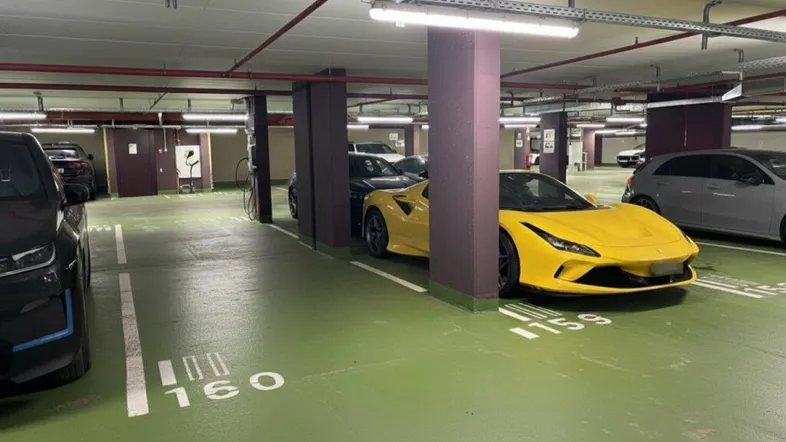 Geräumige Tiefgarage mit mehreren Fahrzeugen, darunter ein gelber Sportwagen, und grüner Bodenmarkierung.