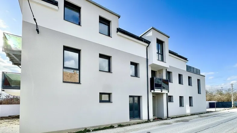 Modernes Mehrfamilienhaus mit weißer und grauer Fassade unter blauem Himmel.