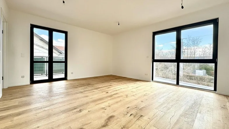 Heller, leerer Raum mit modernem Holzboden und großen Fenstern, die viel Tageslicht hereinlassen.