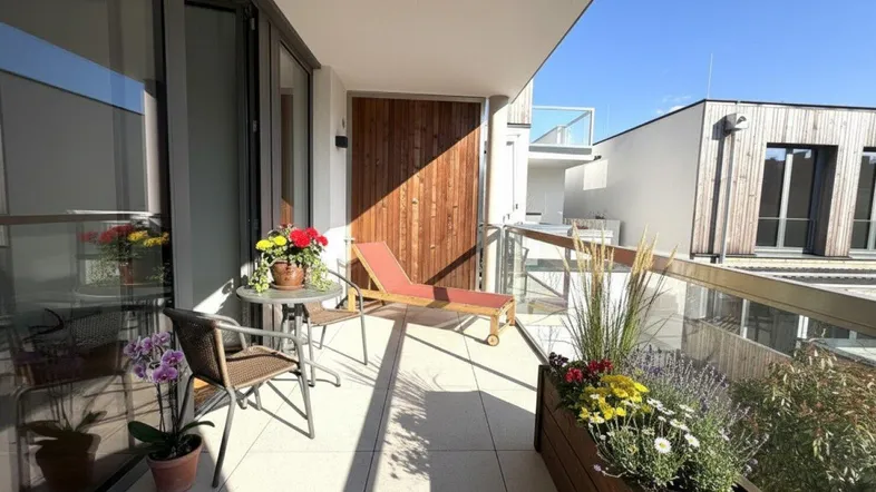 Sonniger Balkon mit Fliesenboden, Glasgeländer und bequemen Gartenmöbeln zum Entspannen.