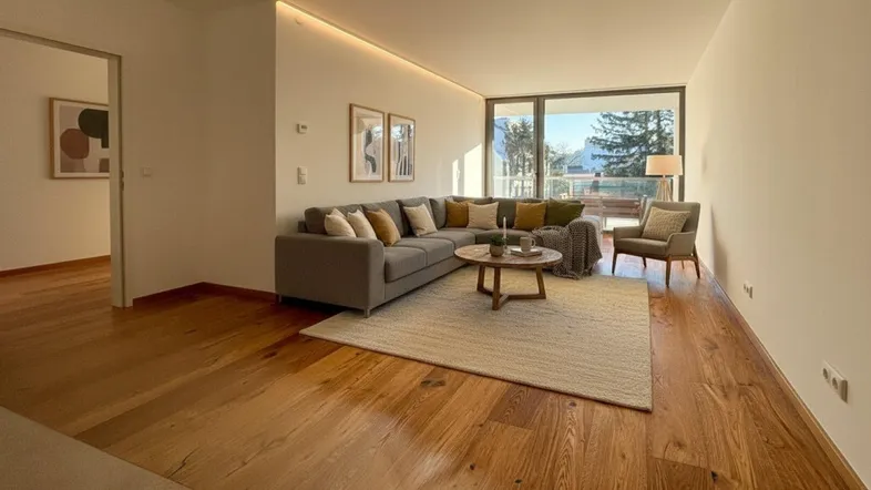 Helles Wohnzimmer mit Holzboden, Ecksofa und großen Fenstern, die viel Tageslicht hereinlassen.