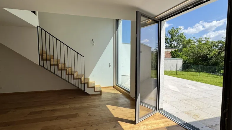 Helles, modernes Zimmer mit Holzboden, offener Treppe und Zugang zu einer Terrasse mit Garten.