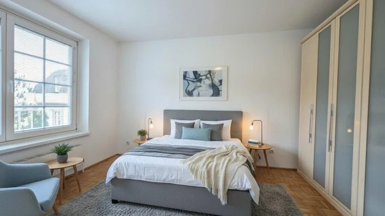 Helles Schlafzimmer mit Parkettboden, großem Fenster und integriertem Kleiderschrank.