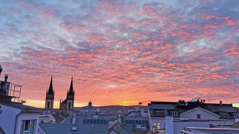 Spektakulärer Sonnenuntergang über der Stadt mit leuchtenden Wolken, Kirchtürmen und urbaner Skyline.