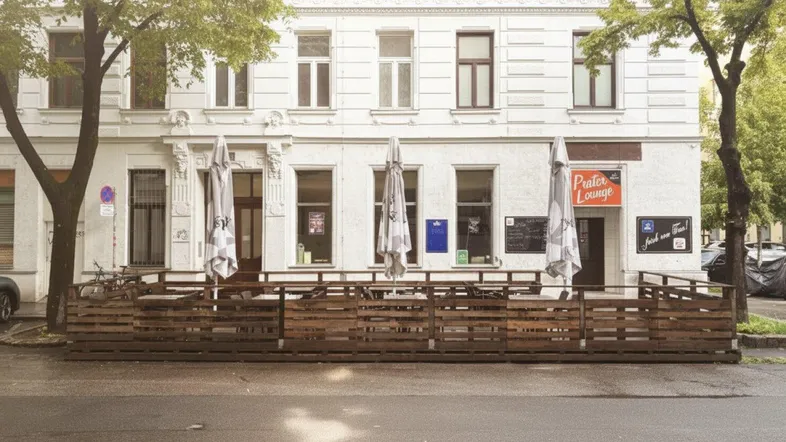 Eine Außenterrasse mit Holzgeländer und Sonnenschirmen vor einem Gebäude mit klassischer Fassade.