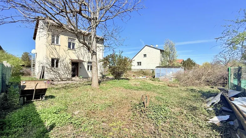 Einfamilienhaus mit großem, naturbelassenem Garten und viel Potenzial für individuelle Gestaltung unter blauem Himmel.