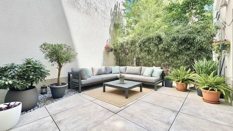 Große, geflieste Terrasse mit bequemen Lounge-Möbeln und üppiger Bepflanzung, ideal zum Entspannen im Freien.