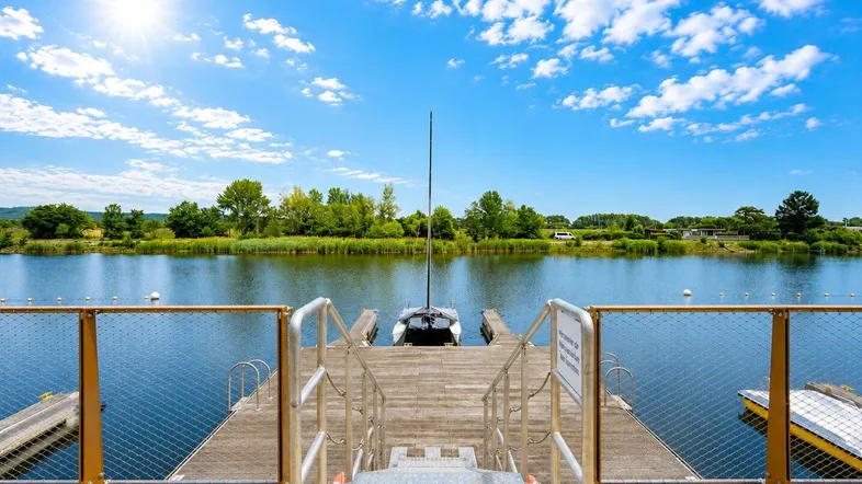 Steg mit Bootsanlegestellen und Blick auf den ruhigen See unter strahlend blauem Himmel.