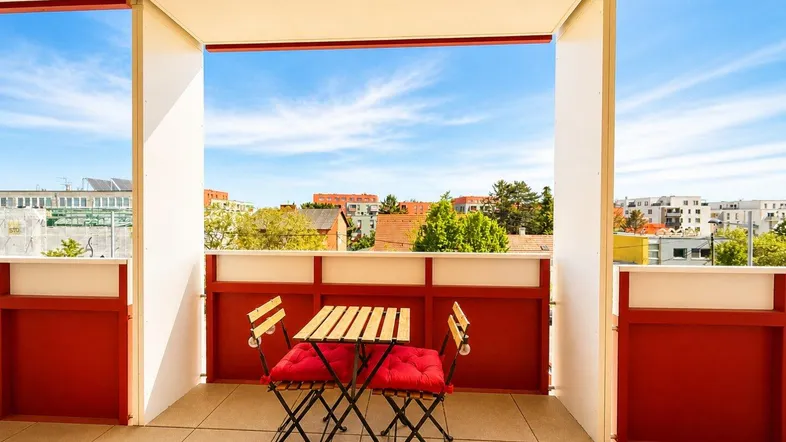 Heller Balkon mit Fliesenboden und rotem Mobiliar, bietet einen weiten Blick über die Umgebung.