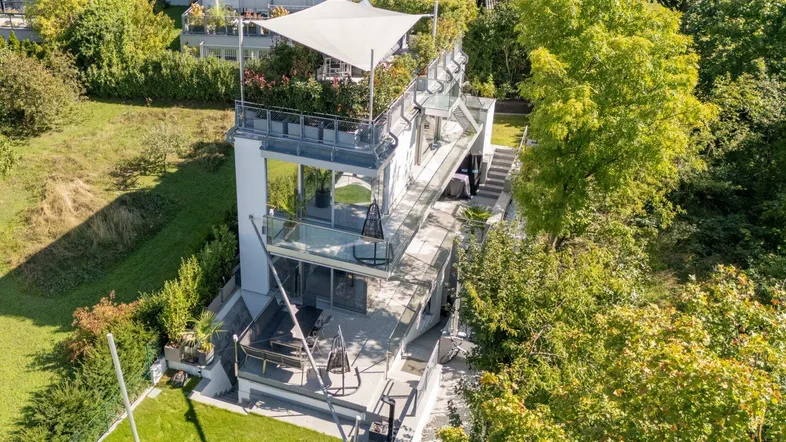 Moderne Architektur mit mehreren Terrassen und Dachterrasse, umgeben von viel Grün.