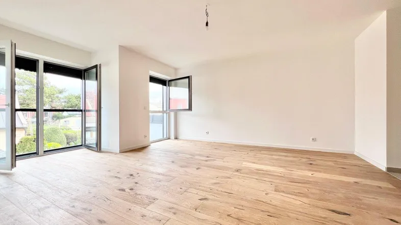 Heller, leerer Wohnraum mit neuem Holzboden und Zugang zu einem Außenbereich.