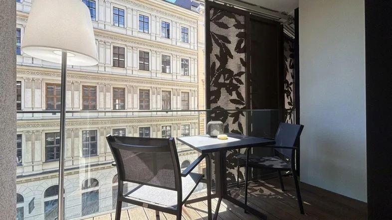 Heller Balkon mit Holzboden, Sitzgelegenheiten und Blick auf historische Gebäude.