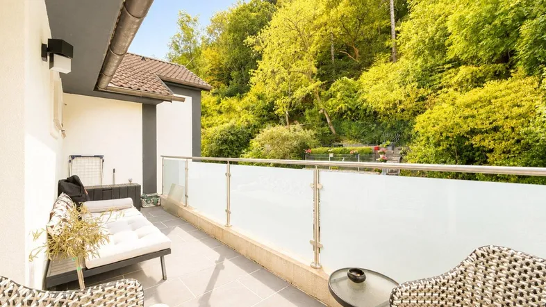 Geräumiger Balkon mit Glasgeländer, Sitzgelegenheiten und Blick ins Grüne.