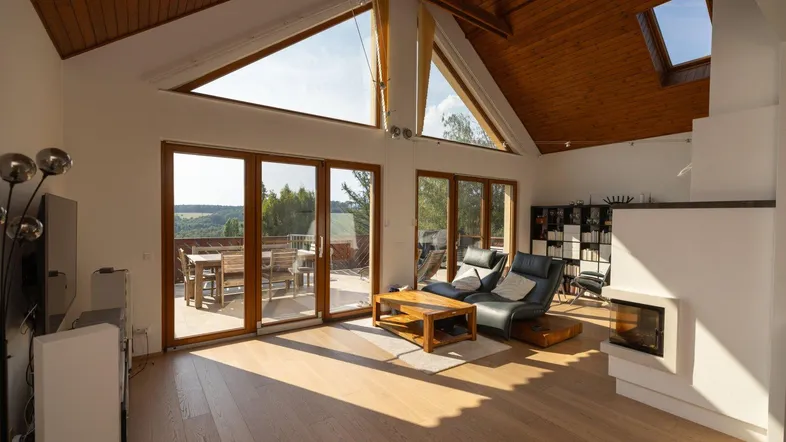 Helles Wohnzimmer mit Holzbalkendecke, Kamin und Zugang zu einer Terrasse mit Weitblick.