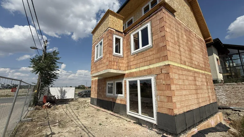 Neubau eines Einfamilienhauses im Rohbauzustand mit sichtbaren Ziegelwänden und Fenstern.
