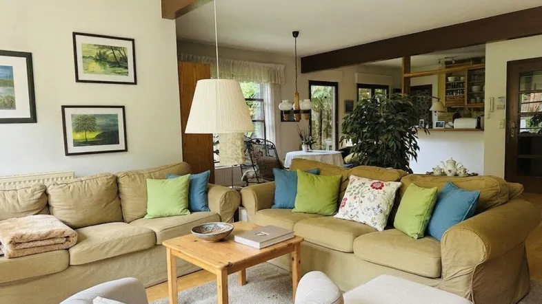 Gemütliches Wohnzimmer mit beigen Sofas, bunten Kissen und Holzbalken, offen zum Essbereich.