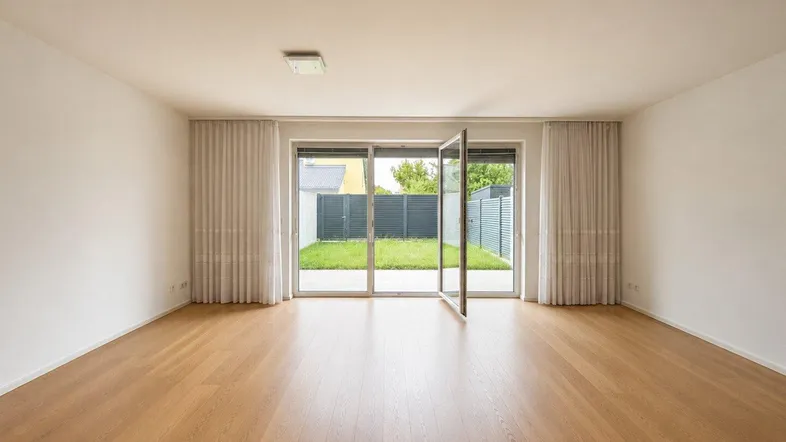 Heller Raum mit Holzboden und großen Glastüren, die zum Garten führen.