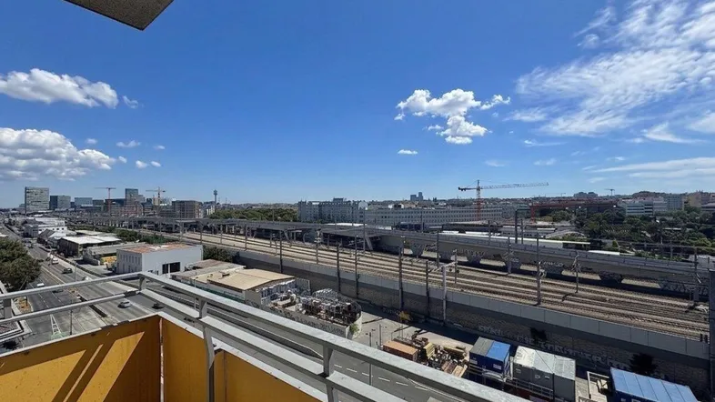 Weitblick über die Stadt mit Bahngleisen und Gebäuden unter blauem Himmel von einem Balkon.