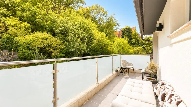 Heller Balkon mit moderner Verglasung, bequemen Liegemöbeln und Blick ins Grüne.