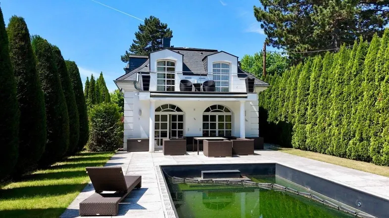 Weißes Haus mit Mansarddach, Terrasse, Pool und gepflegtem Gartenbereich.