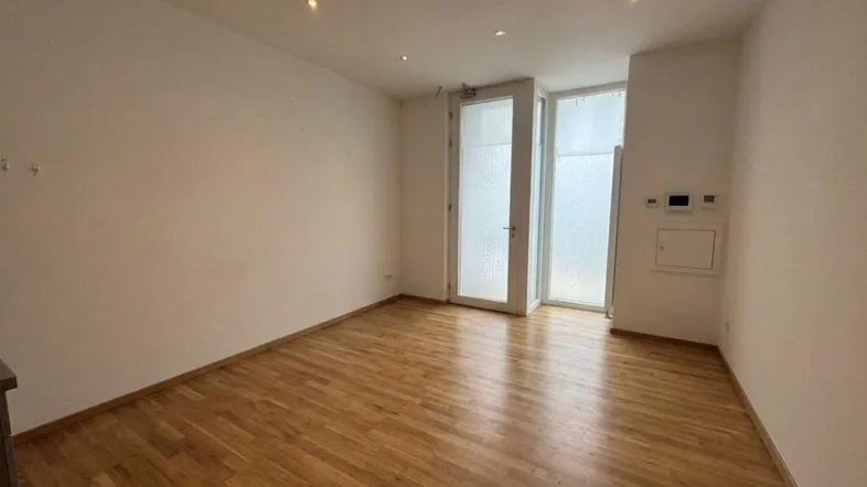 Heller Raum mit Holzboden und großen Fenstertüren, die viel Tageslicht hereinlassen.