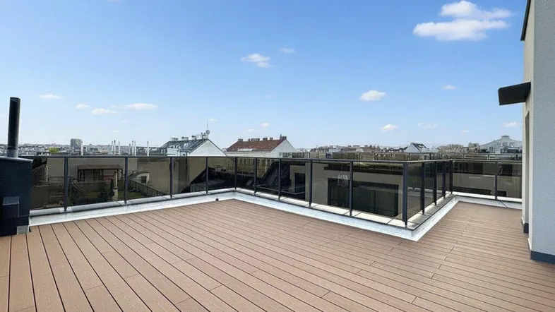 Geräumige Dachterrasse mit Holzdielenboden und Glasgeländer, bietet einen weiten Blick über die Stadt.