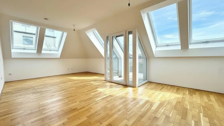 Helles Dachgeschosszimmer mit Parkettboden, schrägen Wänden und mehreren Dachfenstern, die viel Licht hereinlassen.