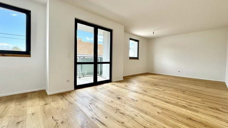 Helles Zimmer mit neuem Holzboden, weißen Wänden und Zugang zu einem französischen Balkon.