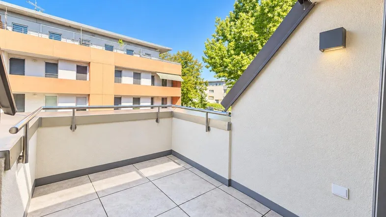 Moderner Balkon mit Fliesenboden und Blick auf umliegende Gebäude und Bäume.
