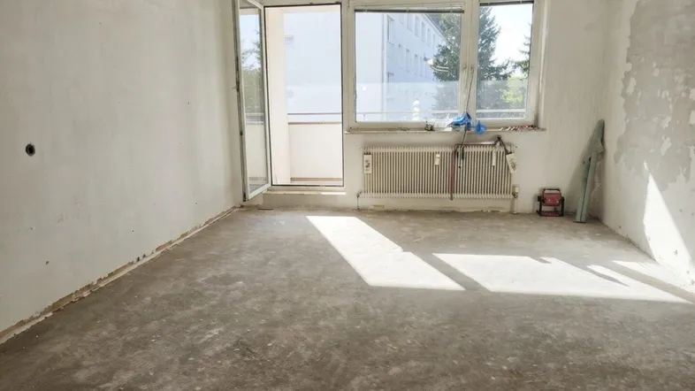 Helles Zimmer im Rohbauzustand mit Zugang zum Balkon und Blick ins Grüne.