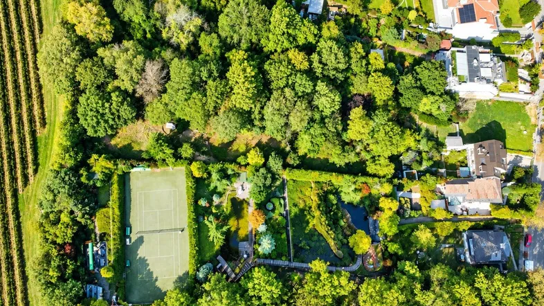 Luftaufnahme eines weitläufigen Anwesens mit Tennisplatz, Teich, üppiger Vegetation und umliegenden Weinbergen.