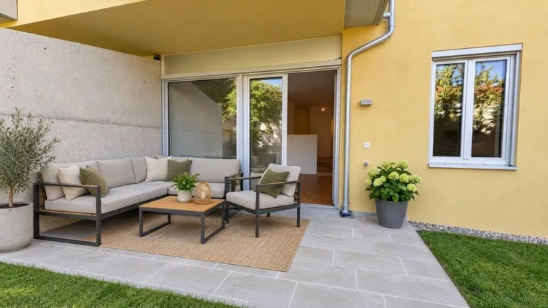 Möblierte Terrasse mit Außenbereich, gefliestem Boden und kleiner Rasenfläche am Neubau.