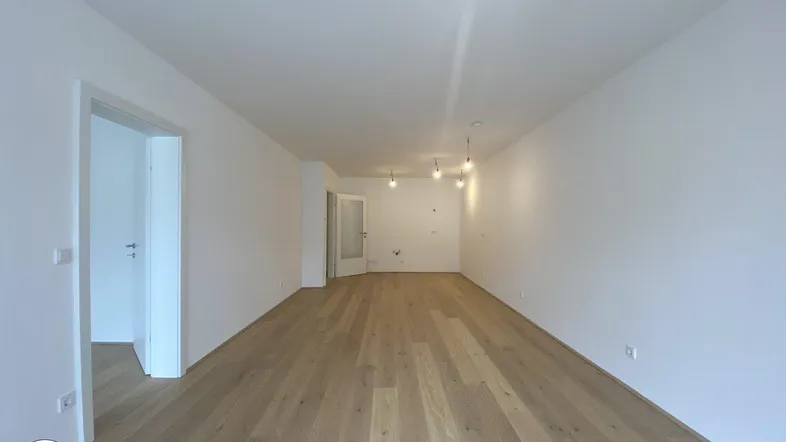 Geräumiges, leeres Wohnzimmer mit hellem Parkettboden und weißen Wänden, bereit zur Einrichtung.