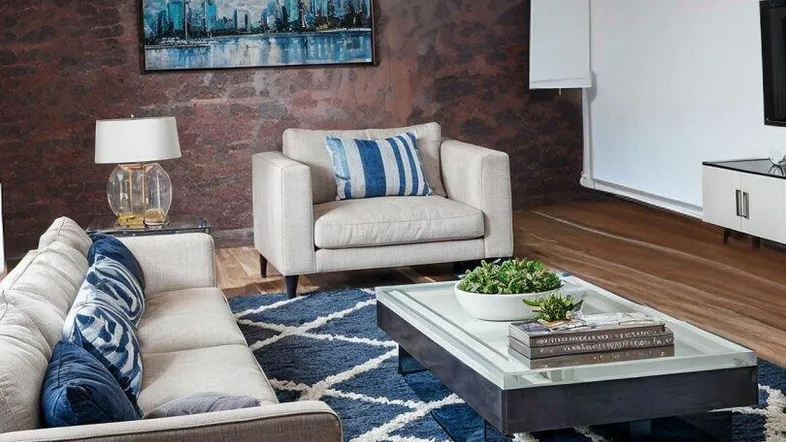 Modernes Wohnzimmer mit beigem Sofa, blauem Teppich und einer strukturierten Akzentwand.